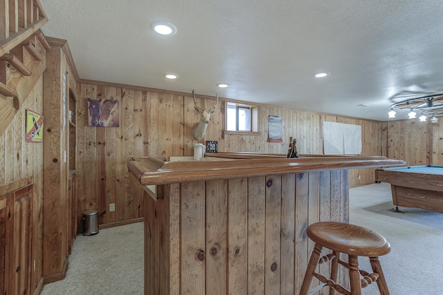 bar with light carpet, wood walls, a textured ceiling, and a bar