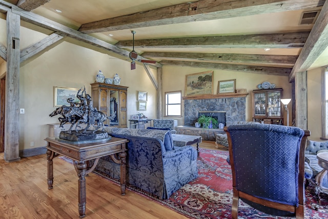 living room with visible vents, lofted ceiling with beams, wood finished floors, a stone fireplace, and ceiling fan