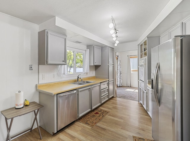 kitchen featuring sink, light hardwood / wood-style flooring, gray cabinets, a textured ceiling, and appliances with stainless steel finishes