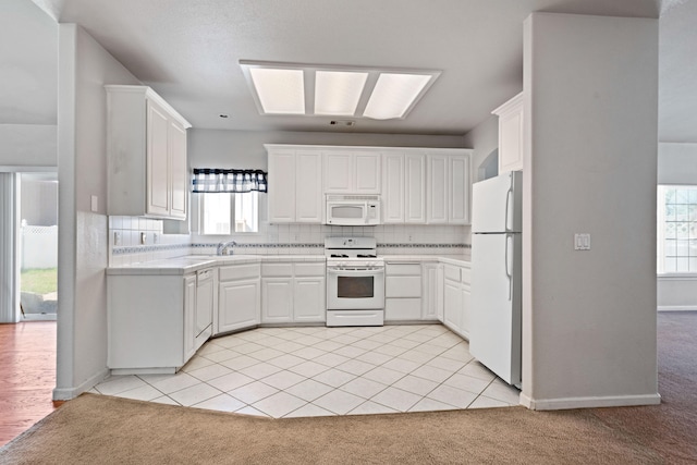 kitchen featuring tasteful backsplash, light carpet, a sink, white cabinets, and white appliances