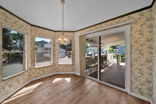 unfurnished dining area featuring hardwood / wood-style floors, a notable chandelier, a healthy amount of sunlight, and crown molding