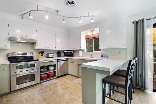 kitchen featuring decorative backsplash, white cabinets, kitchen peninsula, stainless steel appliances, and crown molding