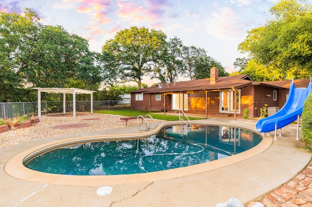 pool at dusk featuring a water slide and a patio area