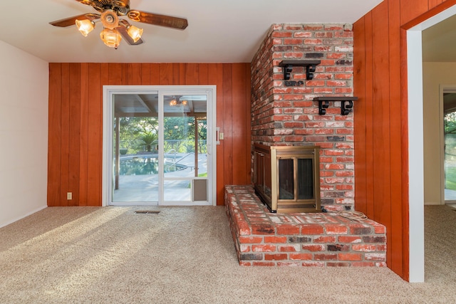 living room with wood walls, ceiling fan, brick wall, carpet flooring, and a fireplace