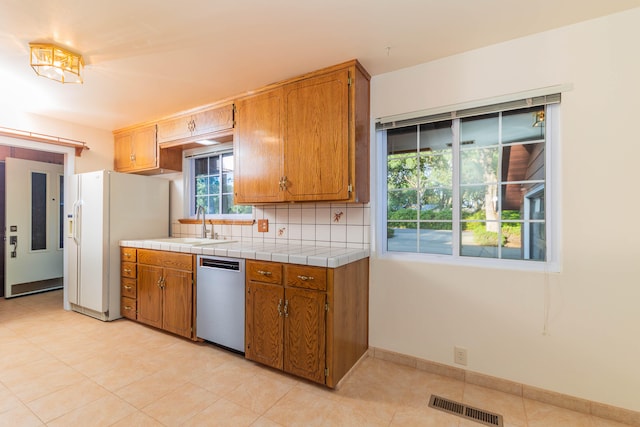 kitchen with dishwasher, backsplash, light tile floors, and tile countertops