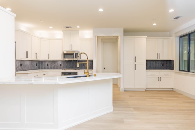 kitchen with backsplash, light stone countertops, light hardwood / wood-style floors, and white cabinetry