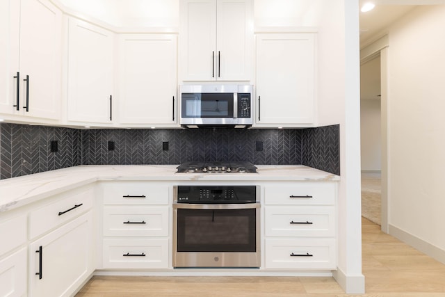 kitchen featuring backsplash, stainless steel appliances, light stone counters, white cabinets, and light wood-type flooring