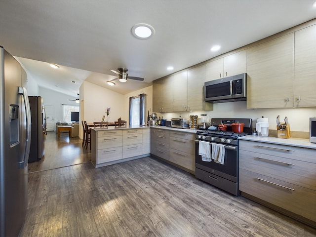 kitchen with appliances with stainless steel finishes, kitchen peninsula, hardwood / wood-style floors, ceiling fan, and vaulted ceiling