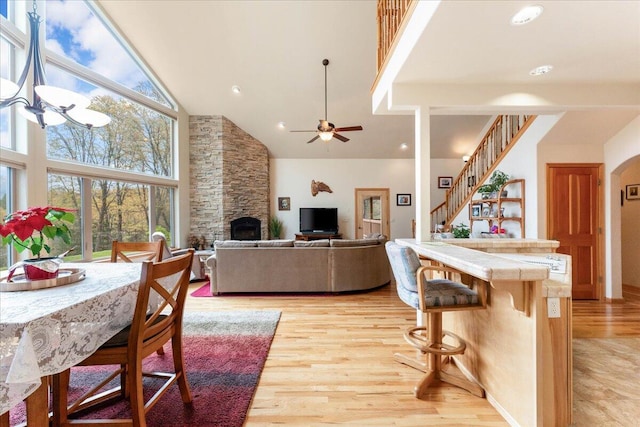 interior space with light hardwood / wood-style flooring, tile counters, a fireplace, ceiling fan with notable chandelier, and high vaulted ceiling