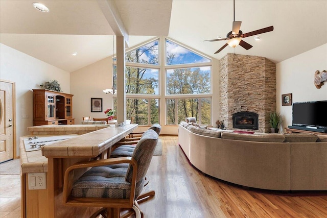 living room with a stone fireplace, high vaulted ceiling, hardwood / wood-style floors, and ceiling fan