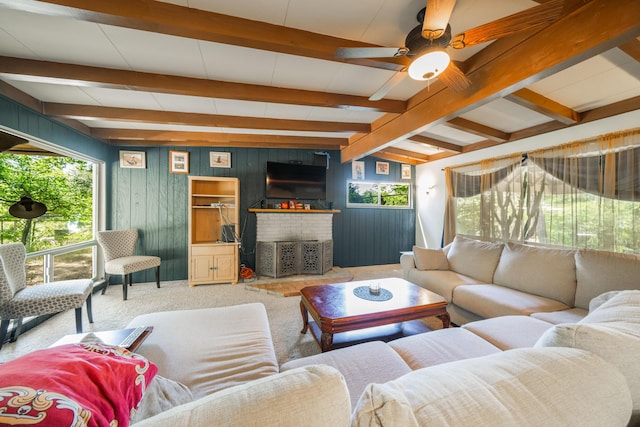 living room with carpet, wood walls, a brick fireplace, vaulted ceiling with beams, and ceiling fan