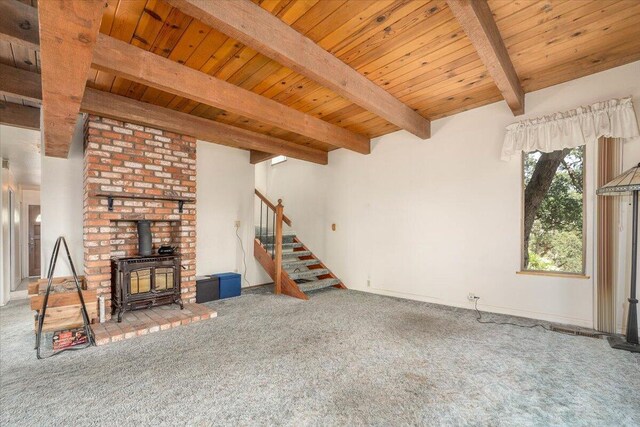 unfurnished living room featuring a wood stove, carpet floors, brick wall, and wooden ceiling