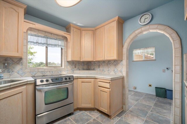 kitchen featuring backsplash, stove, dark tile patterned floors, and light brown cabinets