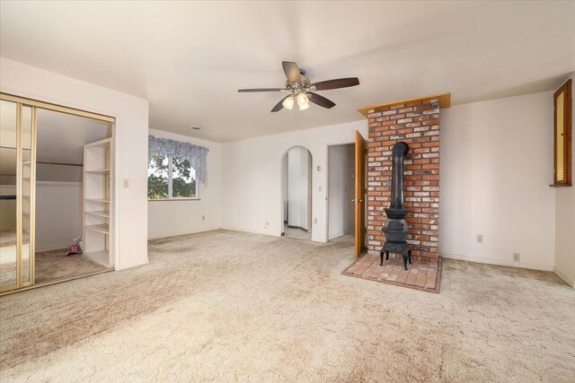 unfurnished living room featuring ceiling fan, a wood stove, light colored carpet, and brick wall