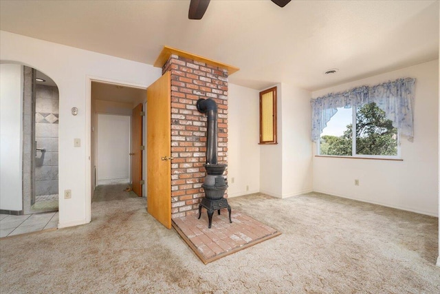 unfurnished living room featuring ceiling fan, a wood stove, brick wall, and carpet