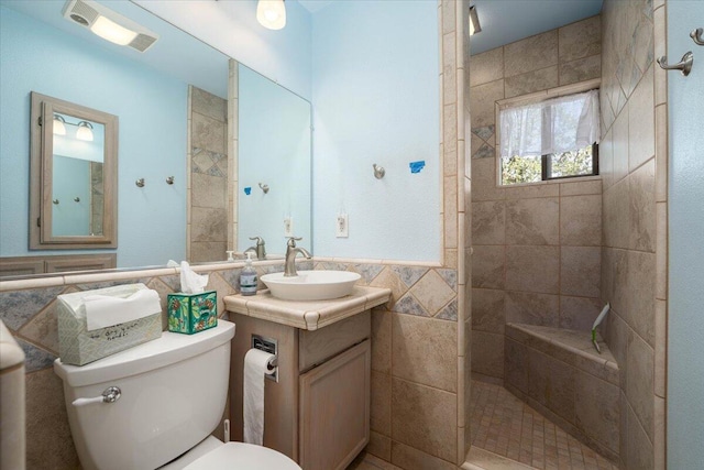 bathroom featuring tile walls, toilet, a tile shower, and vanity