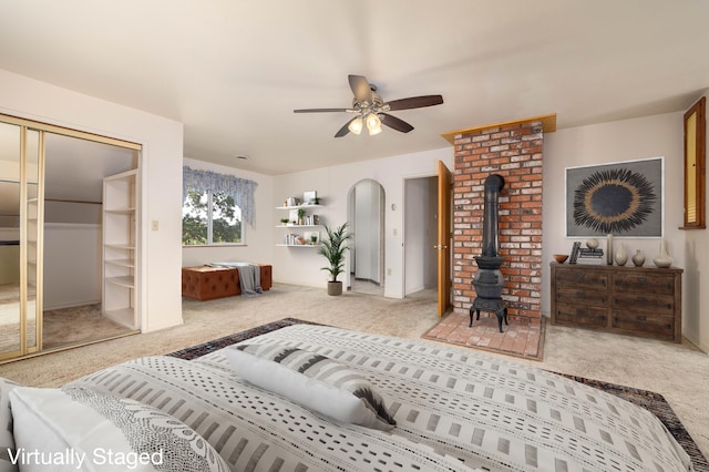 bedroom featuring ceiling fan, brick wall, a wood stove, a closet, and light colored carpet