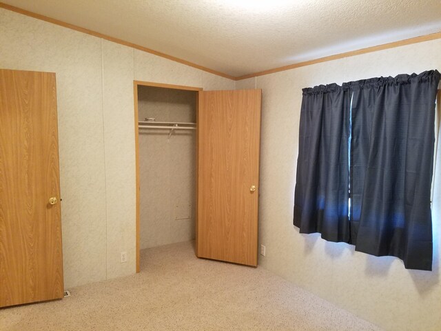 unfurnished bedroom featuring crown molding, a textured ceiling, carpet flooring, and a closet