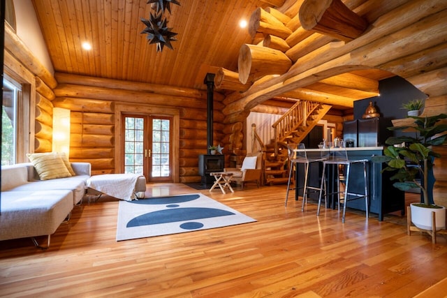 unfurnished living room with light hardwood / wood-style floors, french doors, a wood stove, log walls, and lofted ceiling