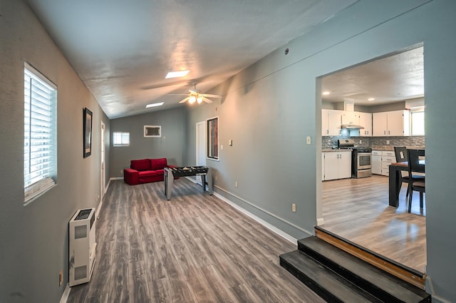 living room featuring vaulted ceiling, wood-type flooring, heating unit, and ceiling fan