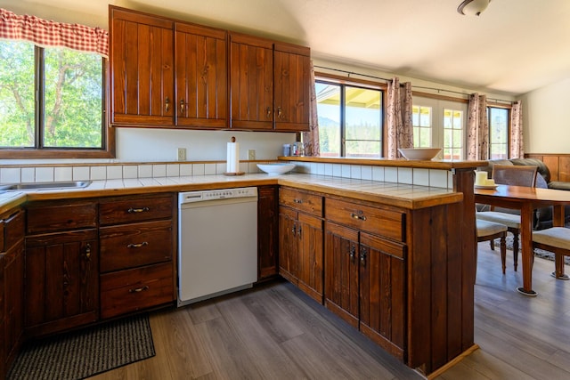 kitchen with kitchen peninsula, tile counters, white dishwasher, and dark wood-type flooring