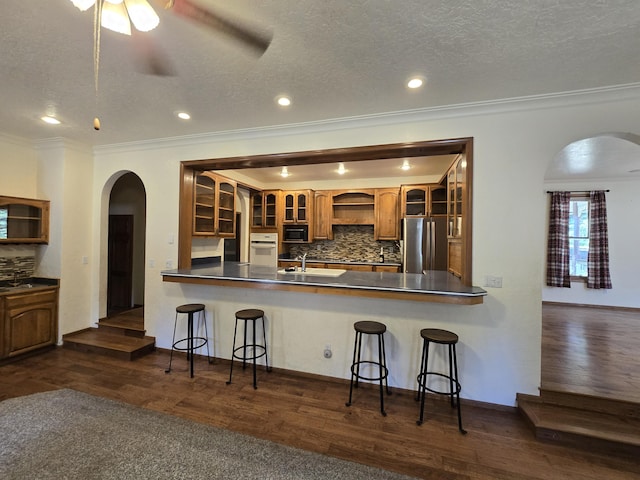 kitchen featuring stainless steel refrigerator, kitchen peninsula, oven, decorative backsplash, and a breakfast bar