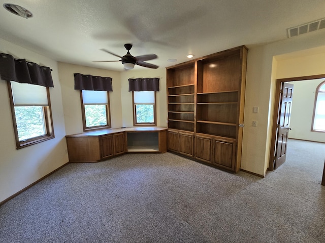 carpeted spare room featuring ceiling fan, built in desk, and a textured ceiling