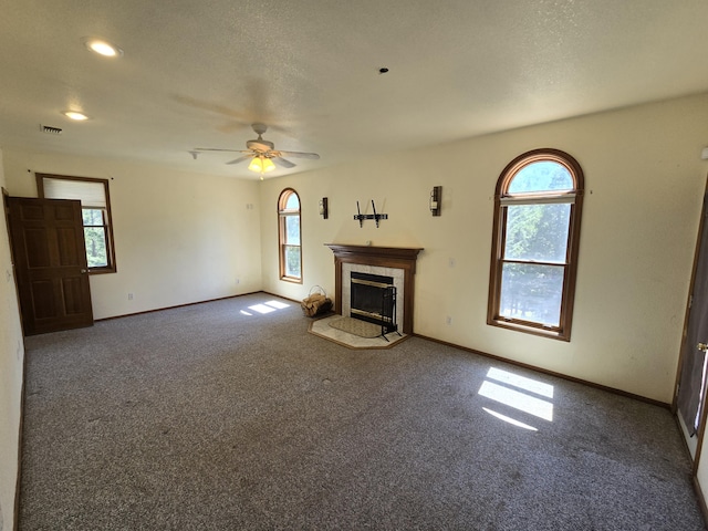 unfurnished living room with ceiling fan, dark carpet, and a tiled fireplace