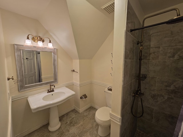 bathroom with a tile shower, lofted ceiling, and toilet