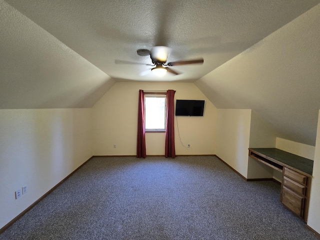 bonus room featuring a textured ceiling, lofted ceiling, dark carpet, and ceiling fan