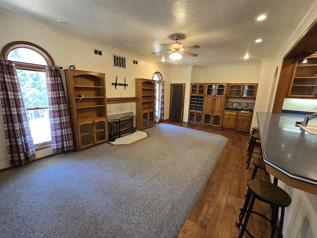 living room featuring ceiling fan, dark hardwood / wood-style floors, crown molding, a textured ceiling, and a fireplace