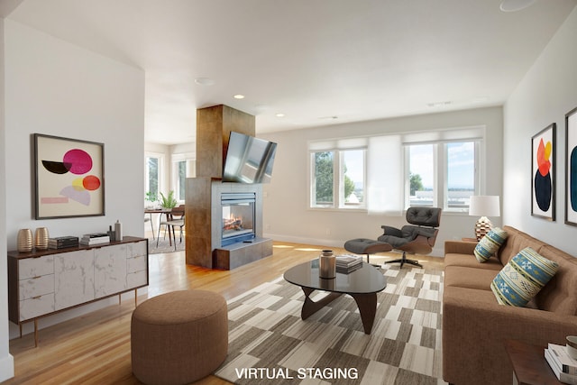 living room featuring light wood-type flooring, a healthy amount of sunlight, and a tiled fireplace