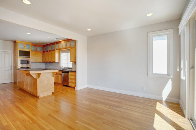 kitchen with appliances with stainless steel finishes, tasteful backsplash, light hardwood / wood-style flooring, a center island, and a breakfast bar area