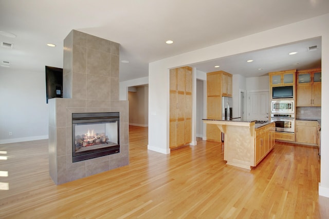 kitchen with a breakfast bar, stainless steel appliances, a tile fireplace, a center island, and light hardwood / wood-style floors