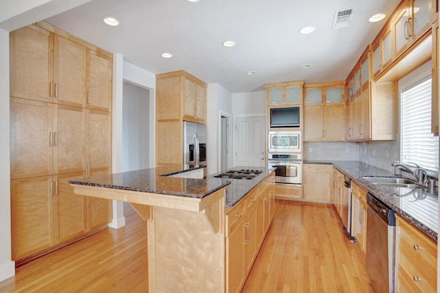 kitchen featuring sink, light hardwood / wood-style flooring, dark stone countertops, a kitchen bar, and appliances with stainless steel finishes