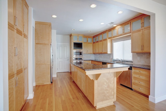 kitchen featuring dark stone countertops, light wood-type flooring, appliances with stainless steel finishes, a kitchen island, and a breakfast bar area