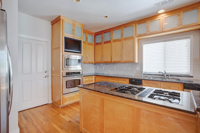 kitchen with sink, stainless steel appliances, backsplash, dark stone counters, and light hardwood / wood-style floors