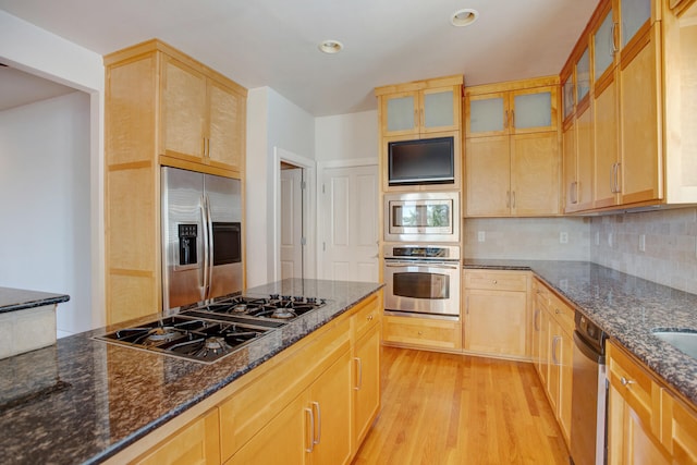 kitchen with tasteful backsplash, built in appliances, dark stone countertops, light hardwood / wood-style floors, and light brown cabinetry