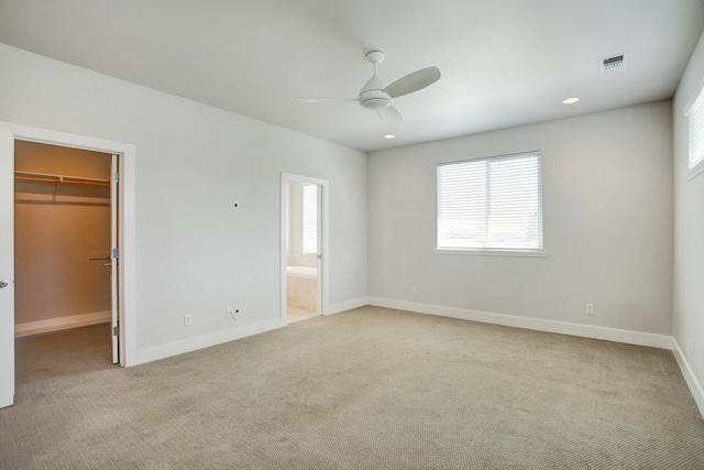 unfurnished bedroom with light colored carpet, a spacious closet, and ceiling fan