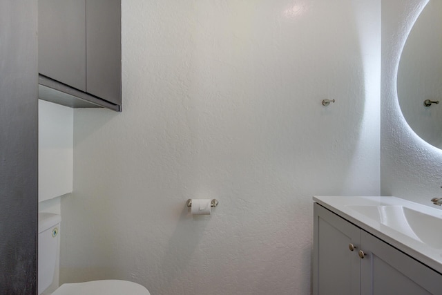 half bathroom featuring toilet, a textured wall, and vanity