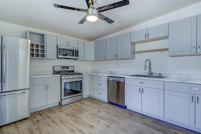 kitchen featuring appliances with stainless steel finishes, a sink, light wood finished floors, light countertops, and vaulted ceiling