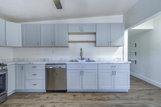 kitchen featuring stainless steel appliances, light stone counters, a sink, and light wood-type flooring