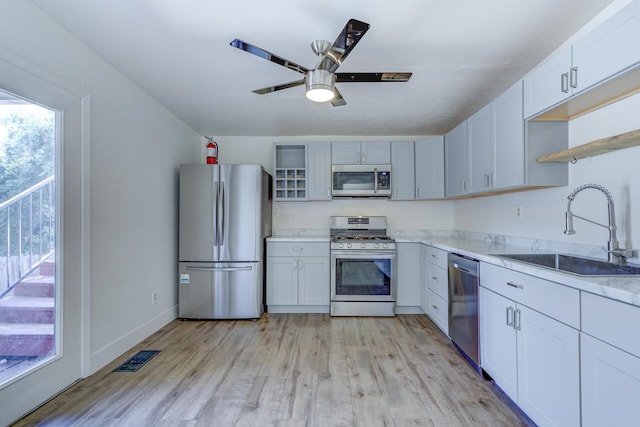 kitchen with a sink, open shelves, stainless steel appliances, and light wood-style flooring