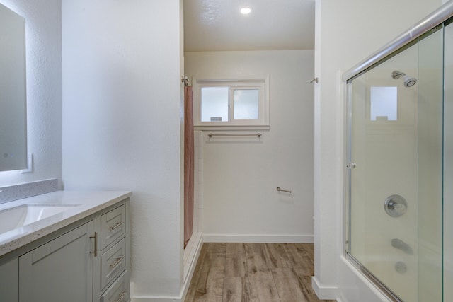 full bath featuring vanity, baseboards, wood finished floors, and shower / bath combination with glass door