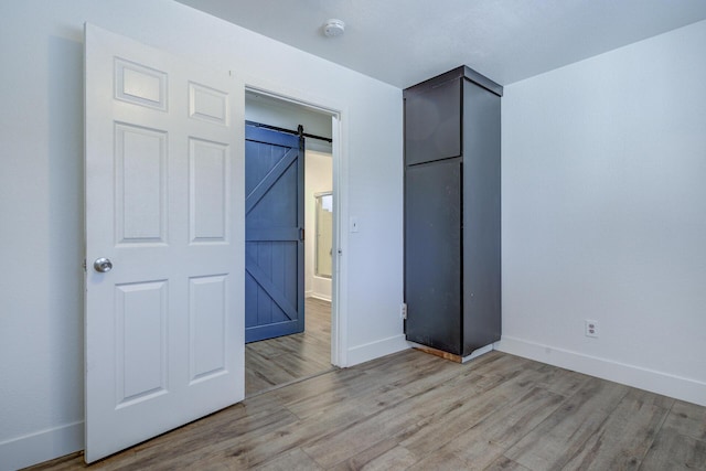 unfurnished bedroom featuring light wood-style floors, a barn door, and baseboards