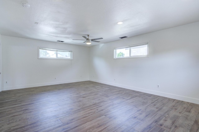 empty room with a healthy amount of sunlight, ceiling fan, wood finished floors, and visible vents