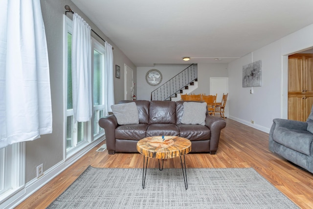 living room featuring baseboards, light wood-style flooring, visible vents, and stairway