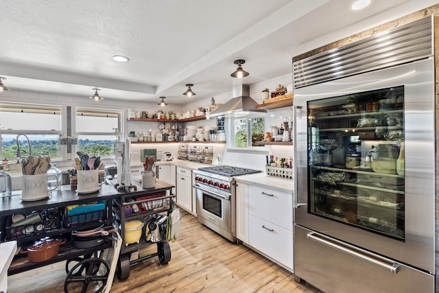 kitchen with backsplash, white cabinets, high end appliances, light wood-type flooring, and wall chimney exhaust hood