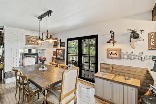 dining area featuring french doors, a brick fireplace, and light wood-type flooring