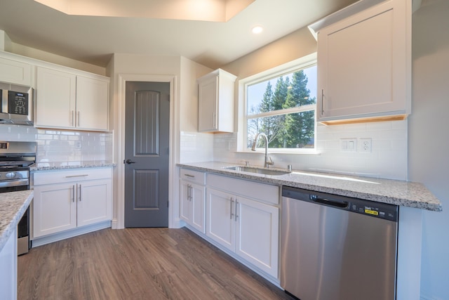 kitchen with stainless steel appliances, dark wood-type flooring, a sink, white cabinets, and light stone countertops